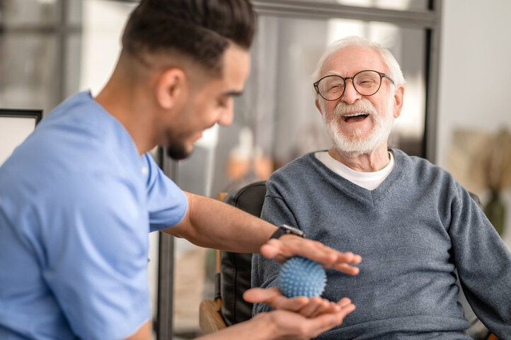 occupational therapist with resident and a exercise ball in his hand smiling